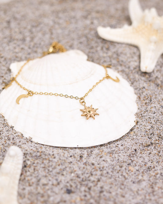 Gold celestial anklet worn on beach foot with sandals and denim