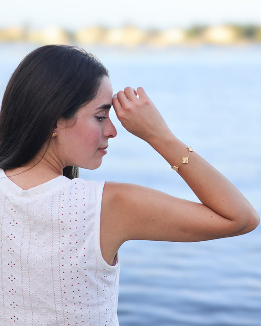 Five gold clover bracelet worn on wrist in beach sunlight
