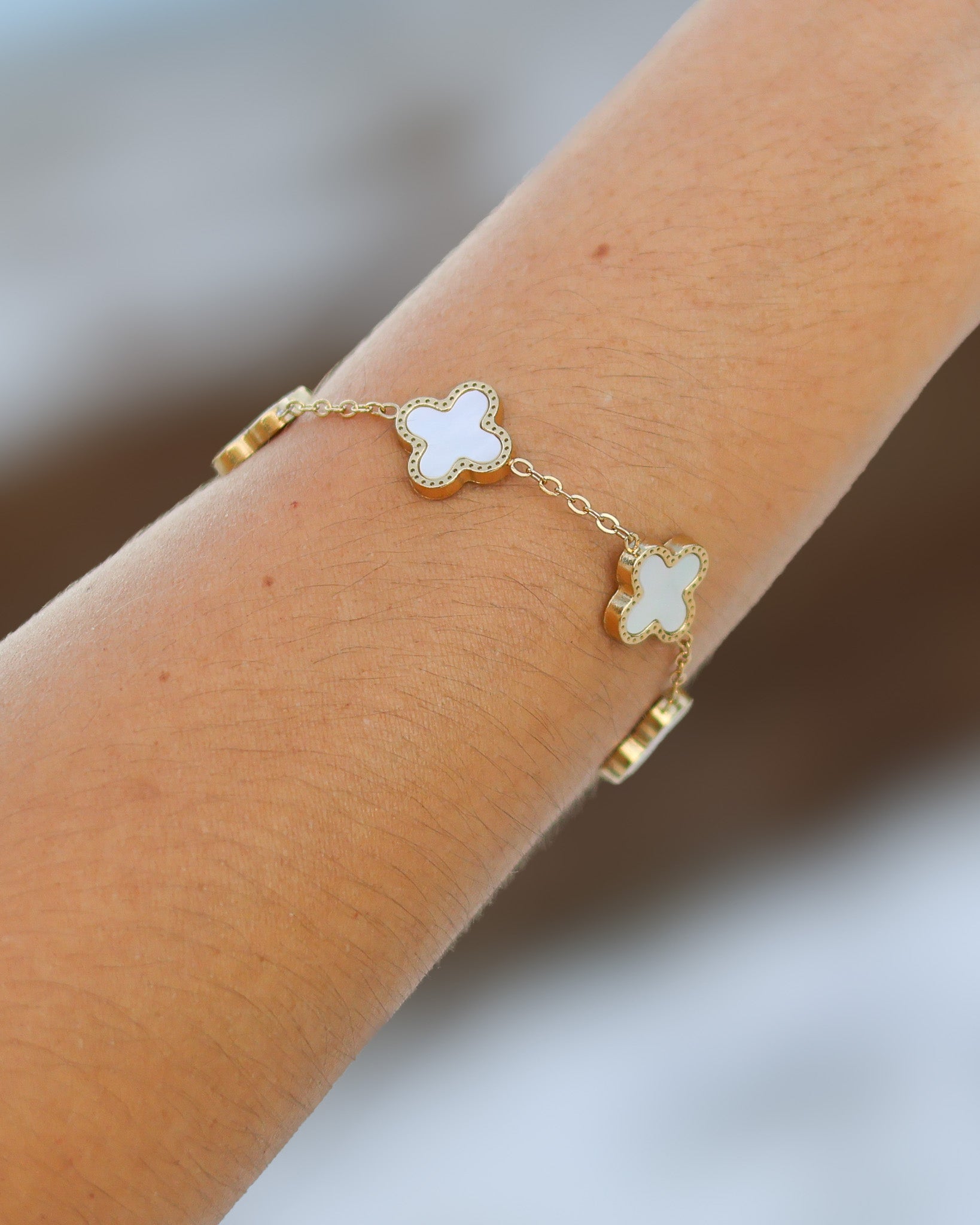 Close-up of white enamel four-leaf clovers on gold chain bracelet