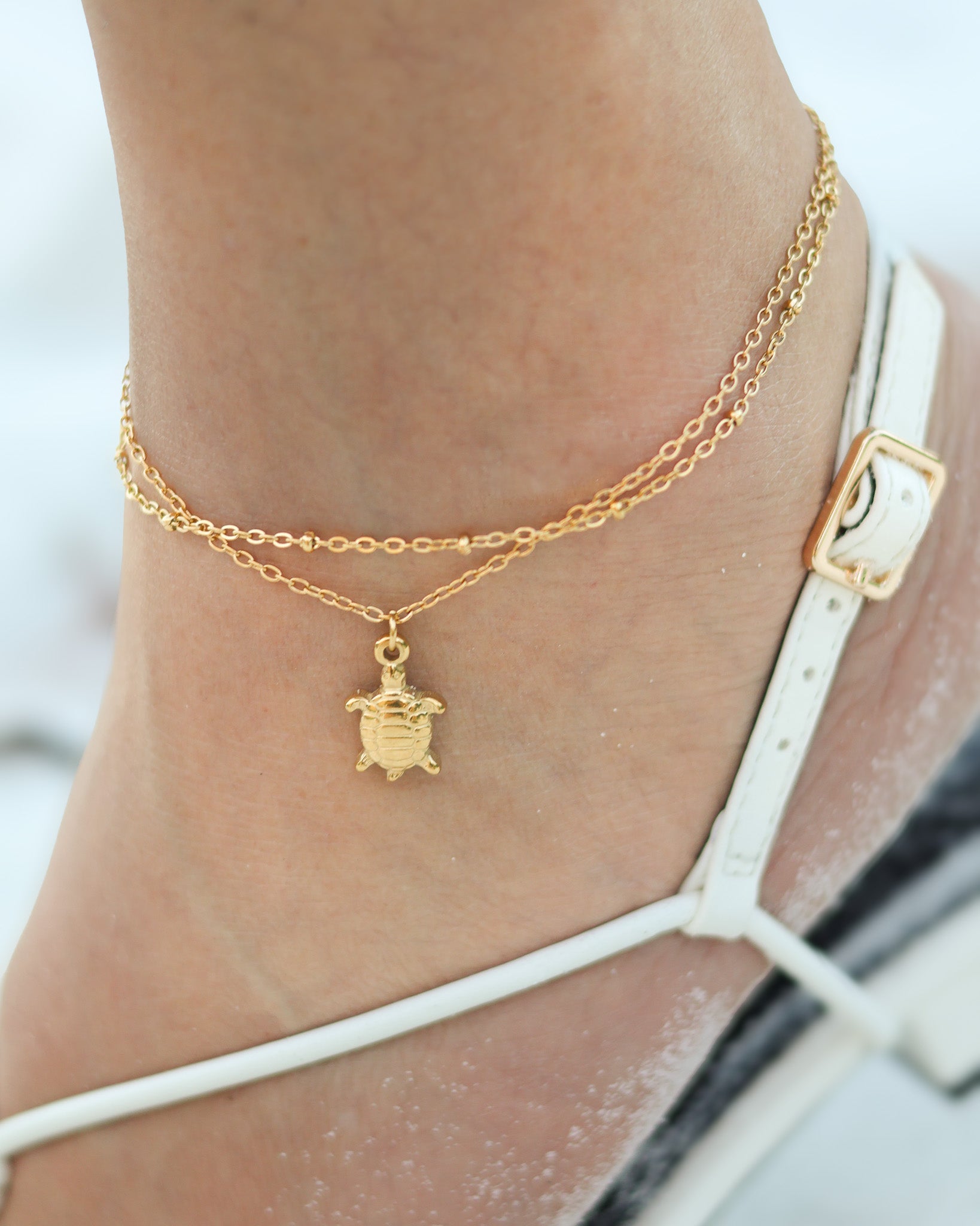 Close-up of 18K gold layered anklet with white beads and turtle charm by Mariarena