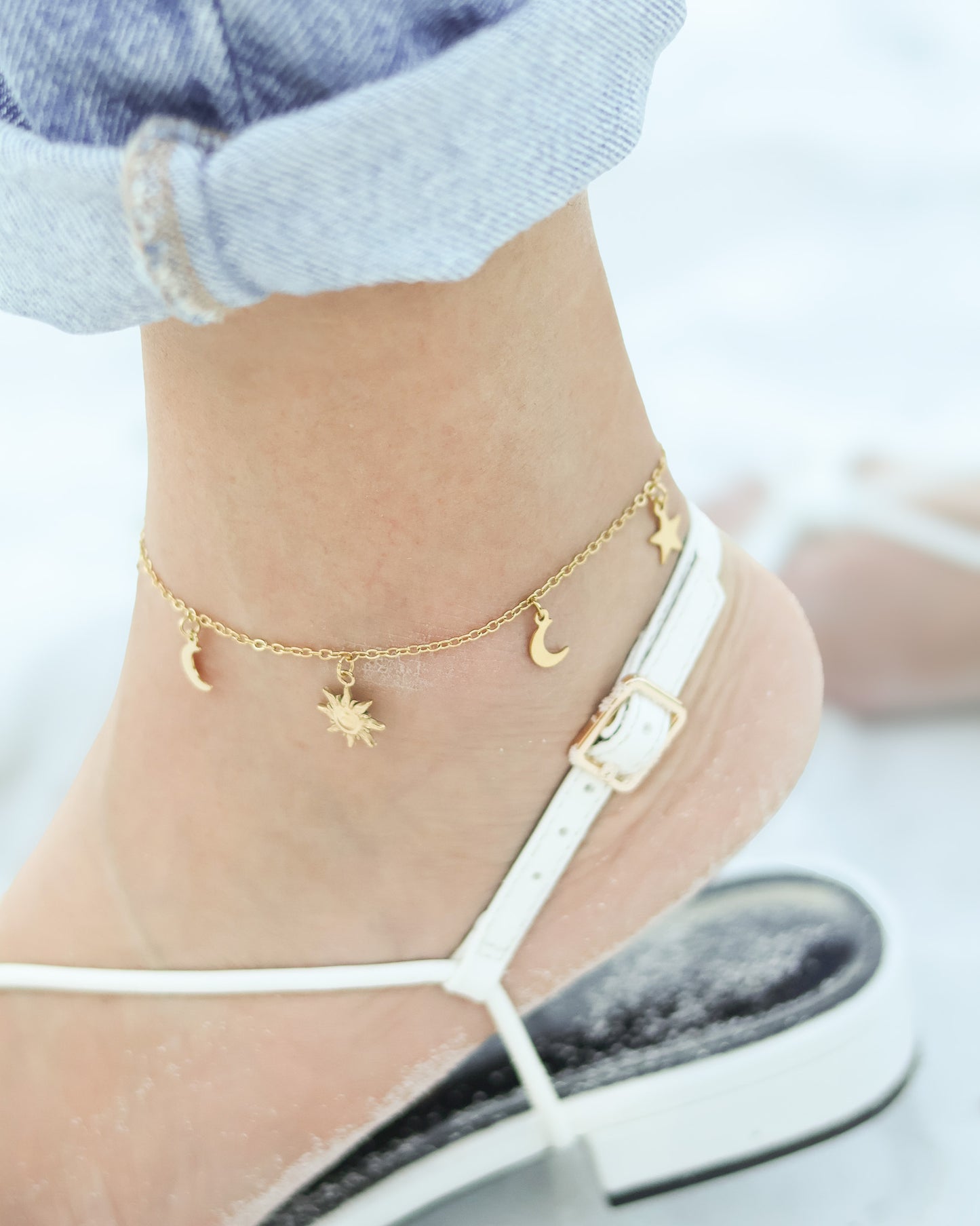 Close-up of sun charm on anklet, placed on shell in the sand