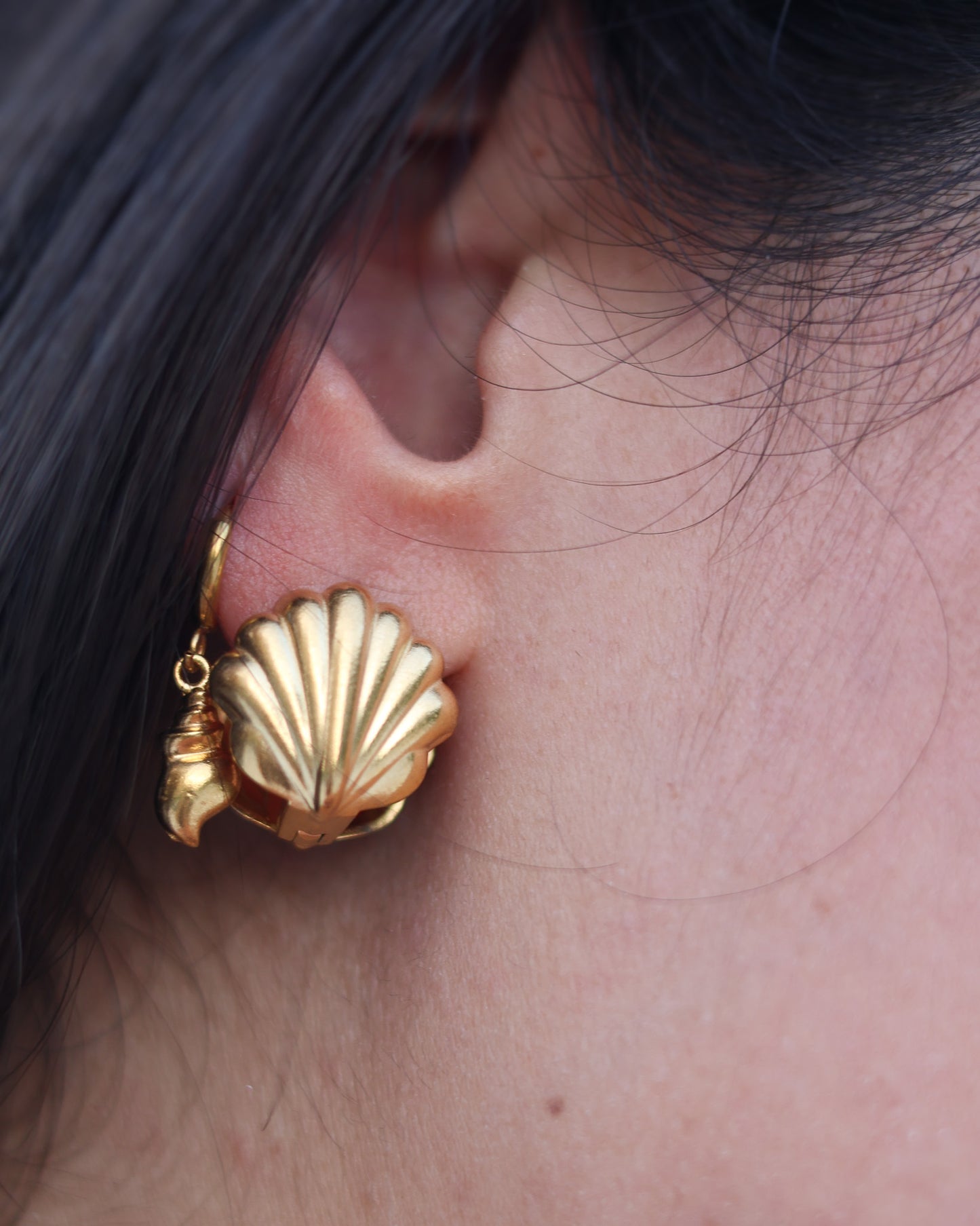 Detailed view of golden seashell earring on model’s ear