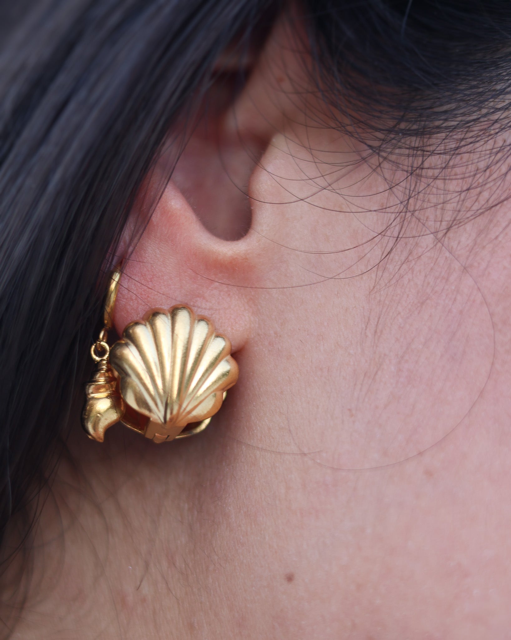 Detailed view of golden seashell earring on model’s ear