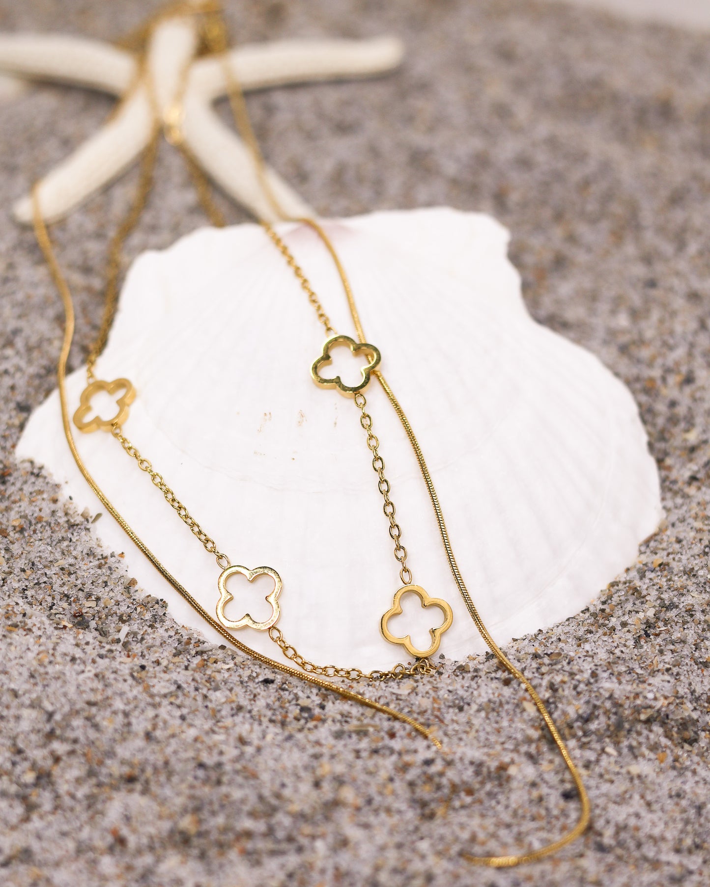 Gold clover necklace displayed on seashell at beach