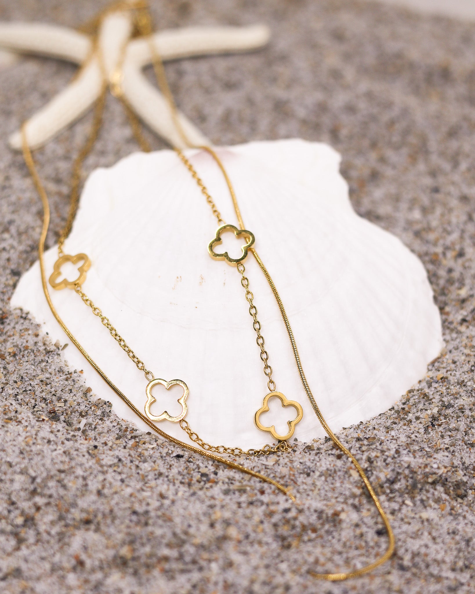 Gold clover necklace displayed on seashell at beach