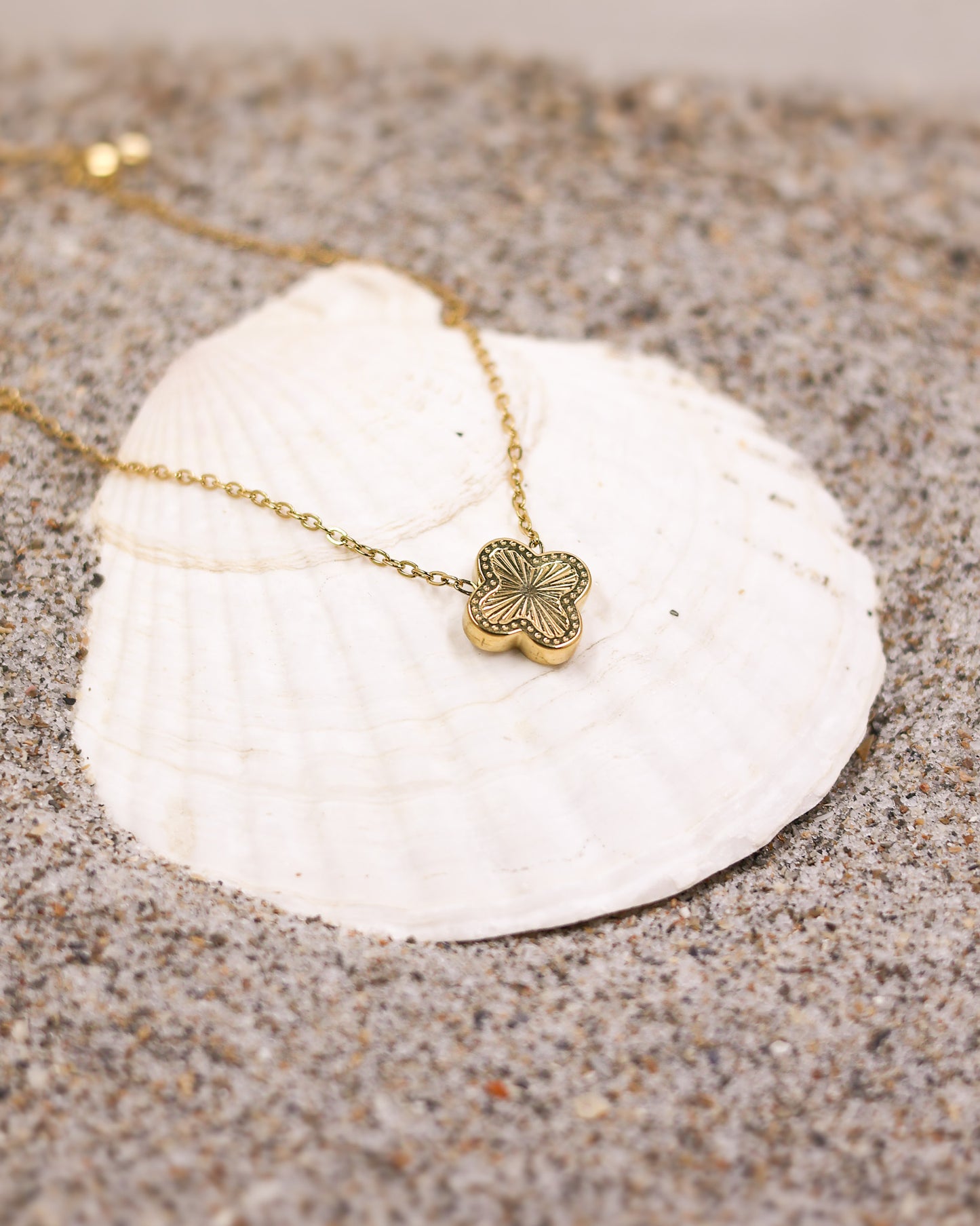 Gold clover necklace resting on a seashell in natural beach setting
