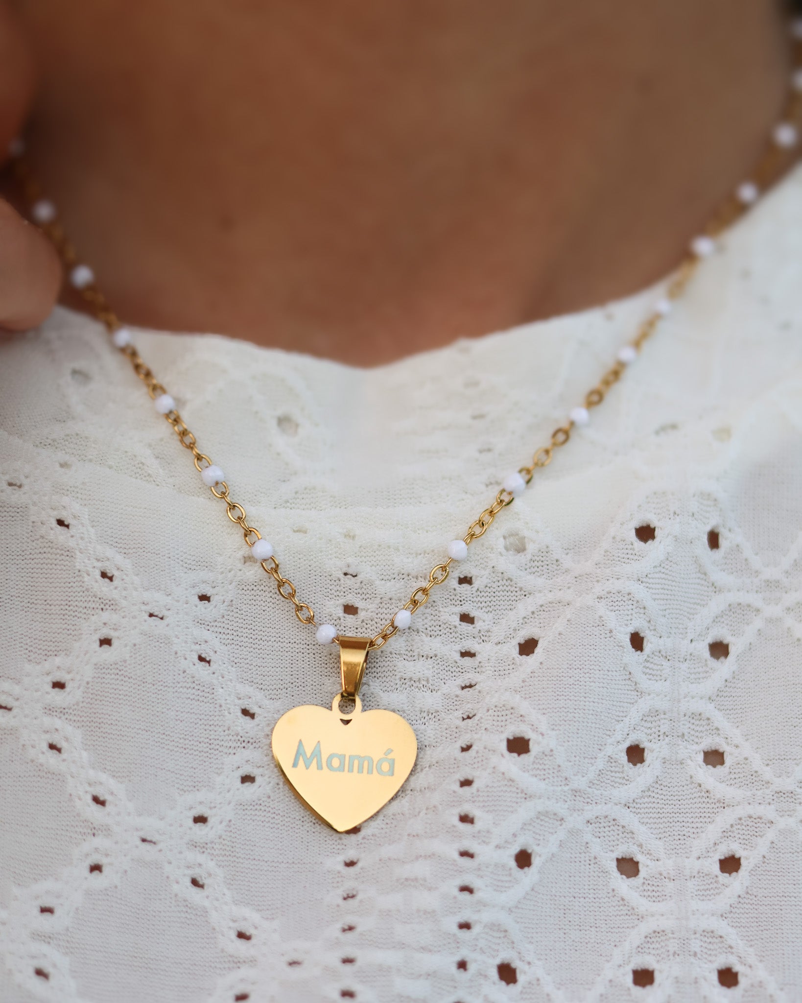 White-beaded chain necklace with engraved gold heart detail styled with natural textures