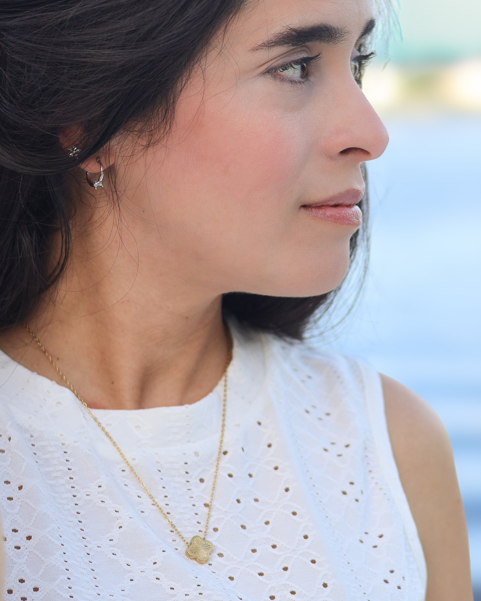 Close-up of woman wearing gold clover necklace near water