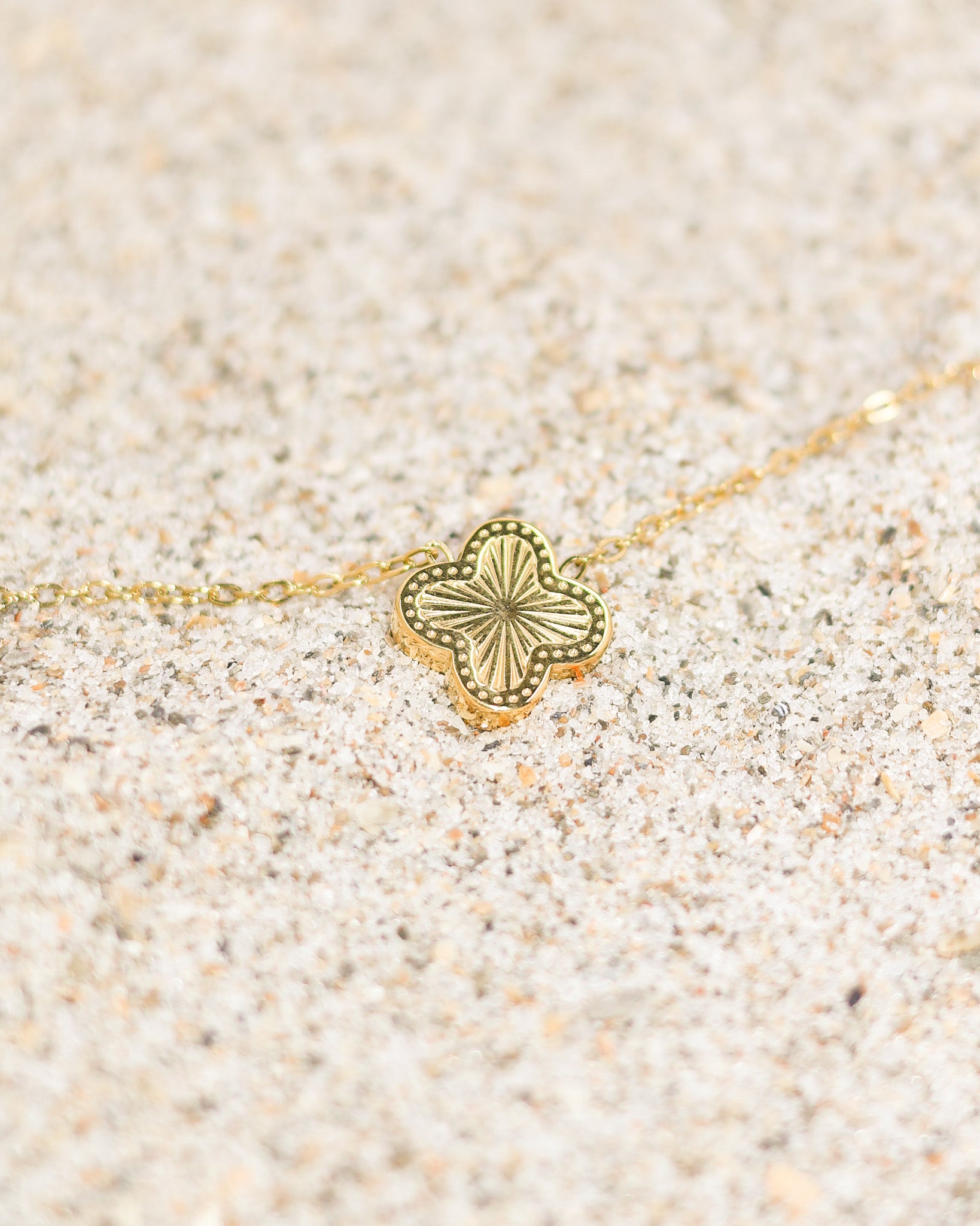 Shining sunburst clover necklace placed on soft beige sand