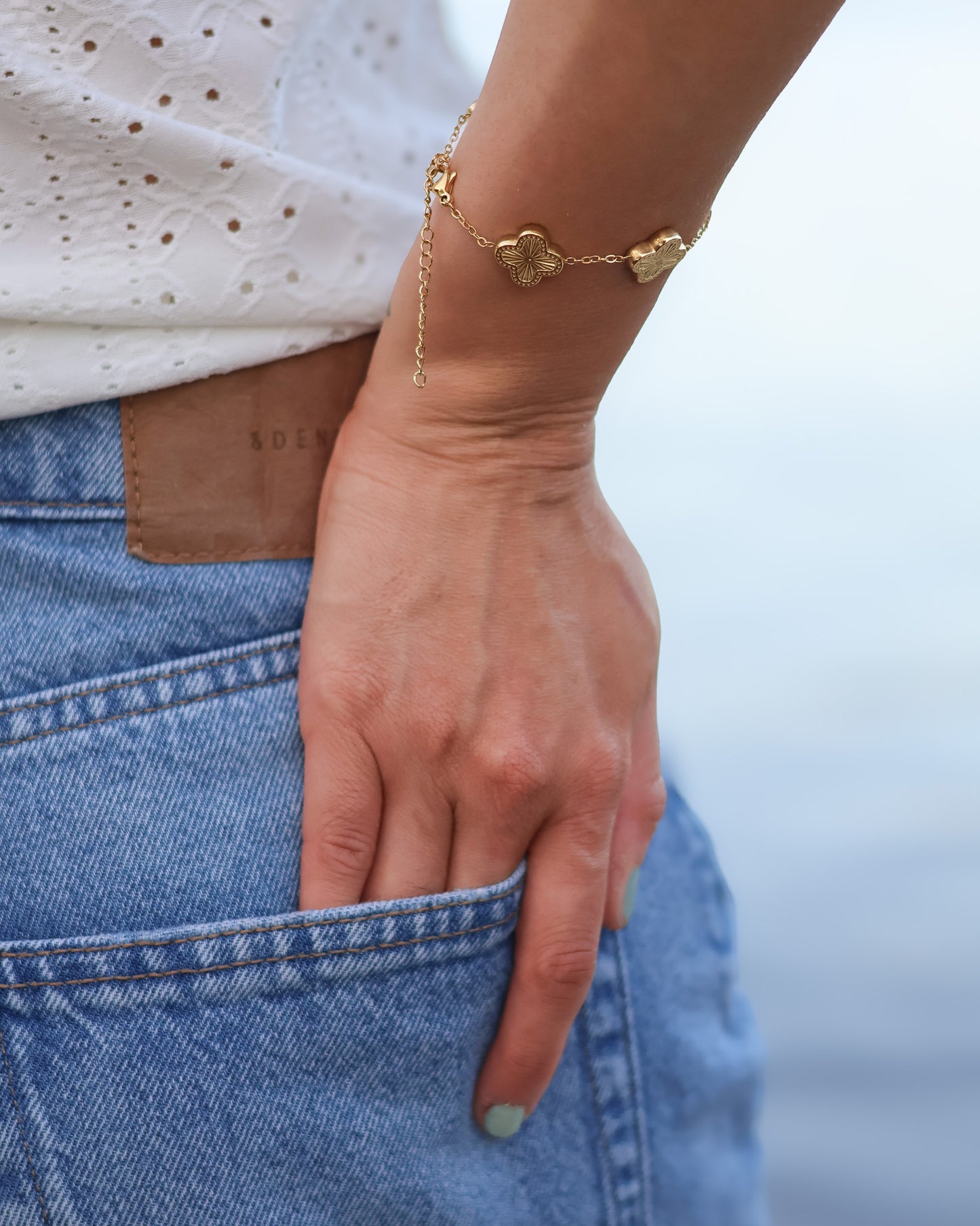 Close-up of a hand wearing a gold bracelet with heart charms, against a blurred background.