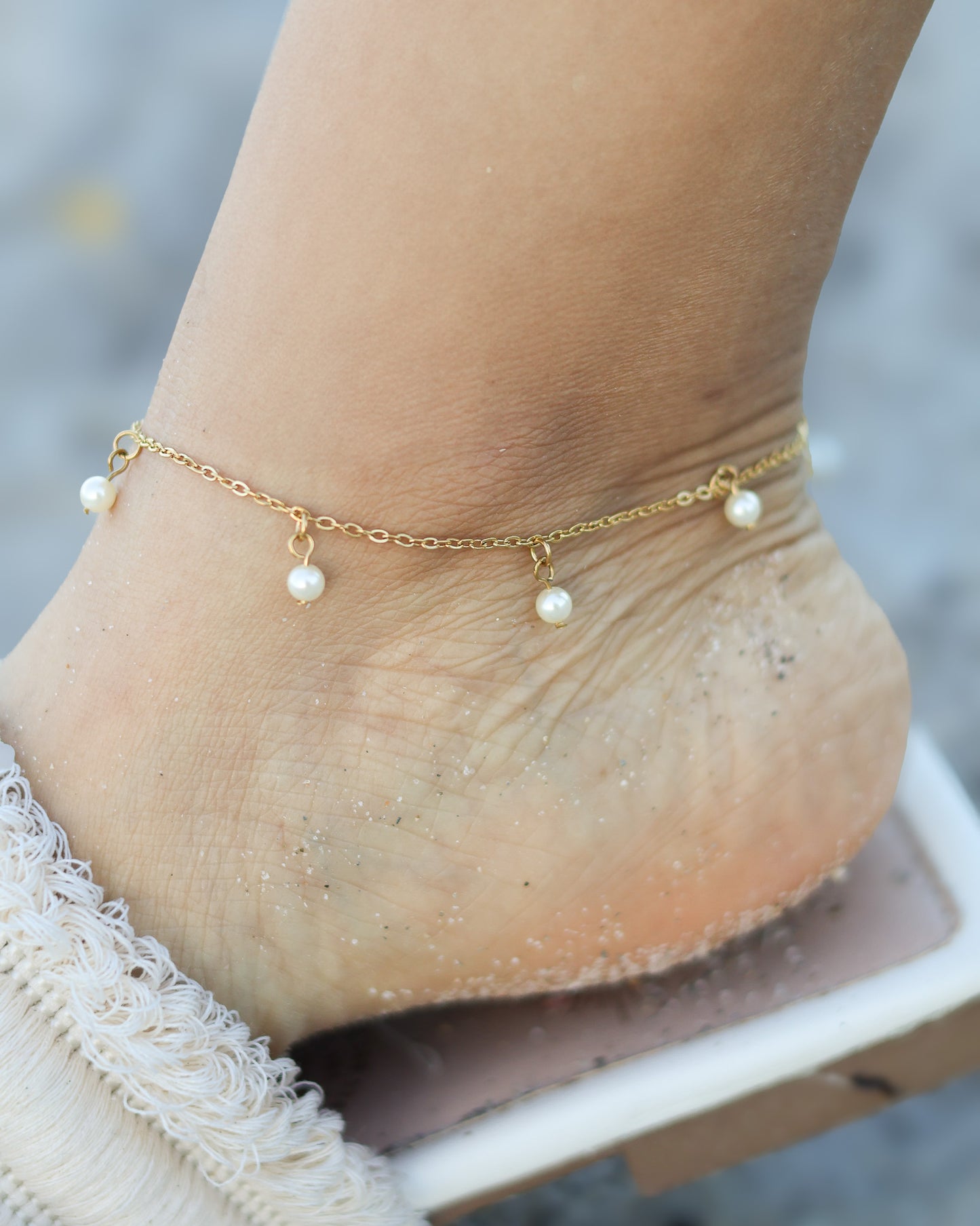 Delicate gold anklet with dangling mini pearls, styled on the beach for a soft and elegant summer look