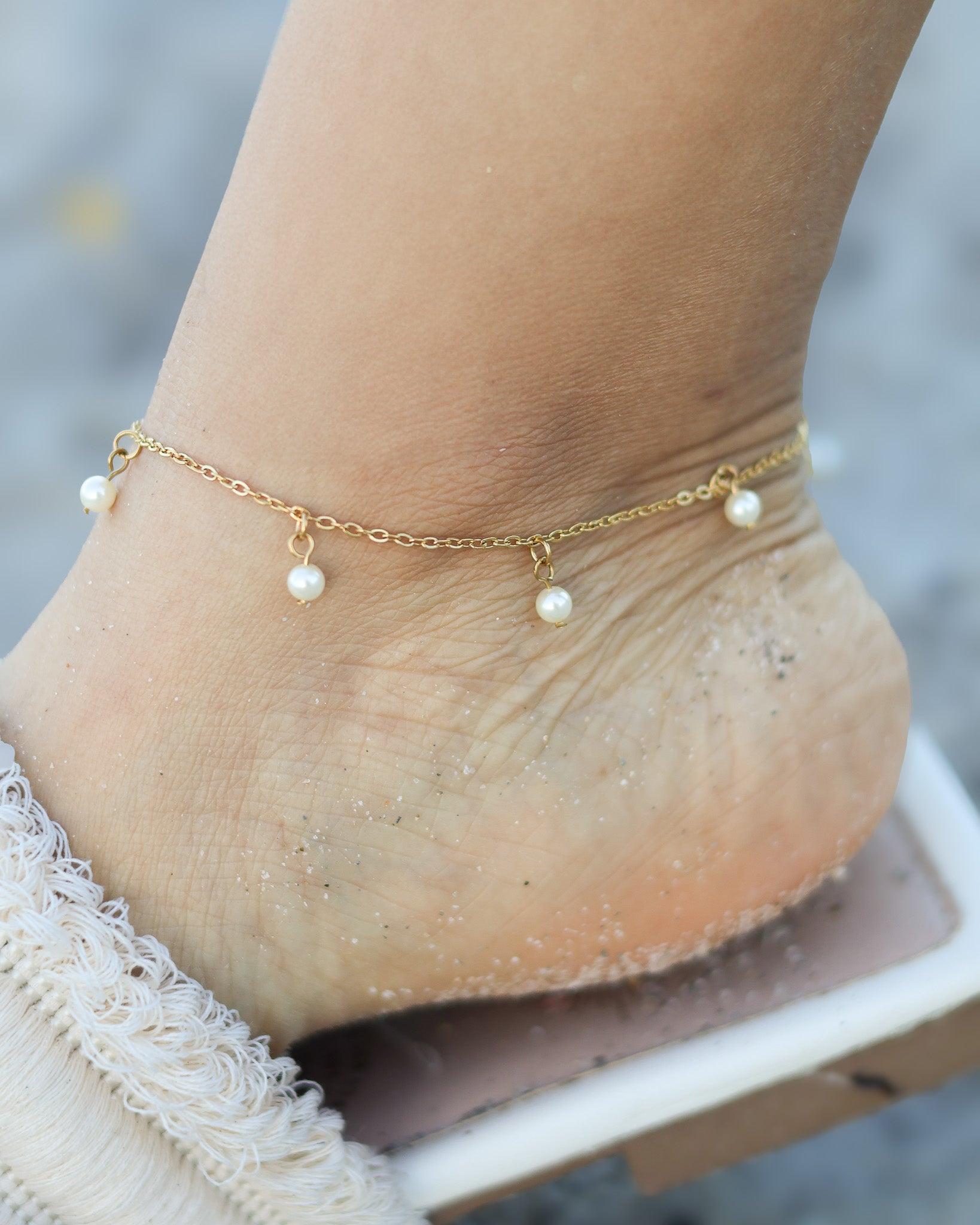 Delicate gold anklet with dangling mini pearls, styled on the beach for a soft and elegant summer look