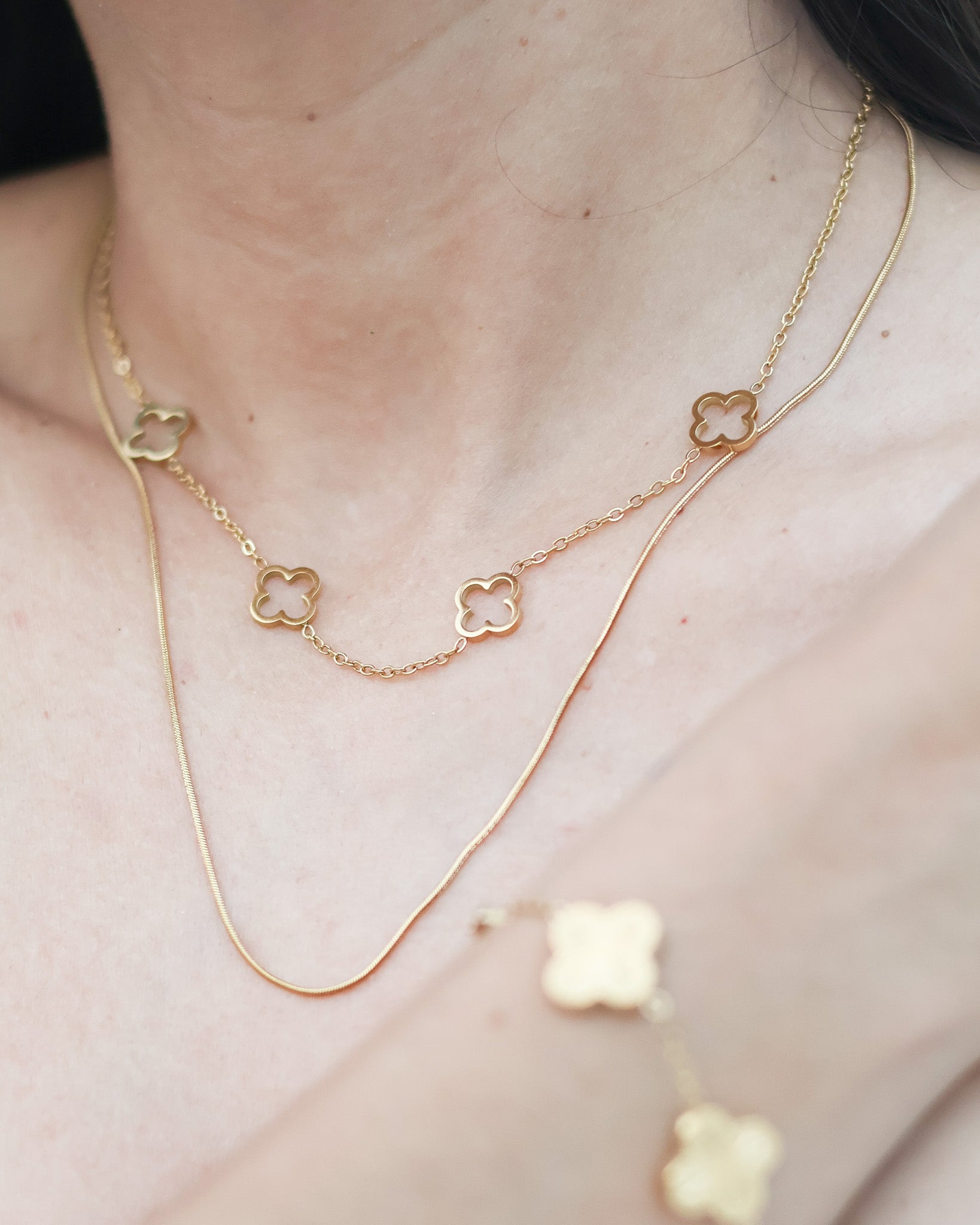 Gold clover layered necklace lying on sand with engraved detail